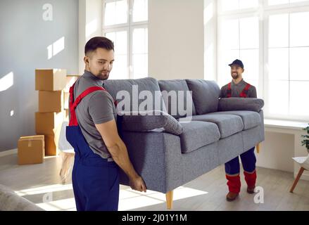 Deux travailleurs professionnels du service de relocalisation dans des salopettes déplacent le canapé dans l'appartement du client. Banque D'Images