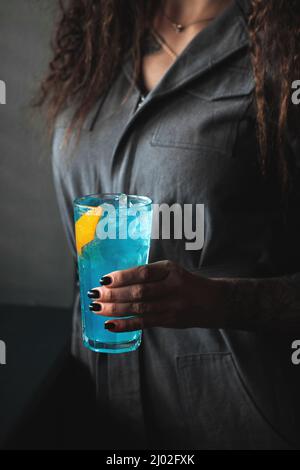 Femme tenant un cocktail bleu dans une balle haute avec de la glace Banque D'Images