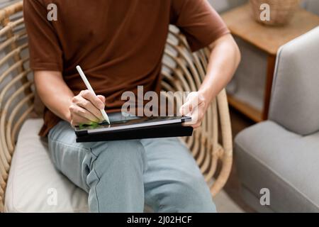 Concept de technologie le jeune homme qui est assis sur la chaise tenant son iPad et notant quelque chose sur lui. Banque D'Images