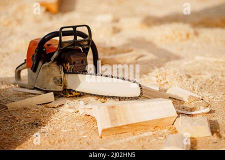 La tronçonneuse sur le chantier de construction de maisons en bois en rondins repose sur fond de sciure. Banque D'Images