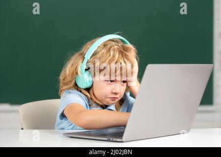 Un enfant triste en colère dans un casque à l'aide d'un ordinateur portable et étudier en ligne avec un professeur d'appel vidéo à l'école. Peu drôle administrateur système ou programmeur. Banque D'Images