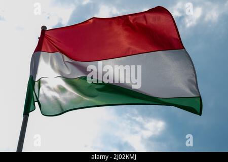 Drapeau hongrois agitant sous le vent et la lumière du soleil. Drapeau de Hongrie sur fond bleu ciel. Banque D'Images