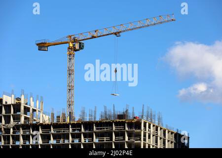 Grue à tour de construction avec cargaison au-dessus du bâtiment résidentiel non fini sur fond bleu ciel. Construction de logements, ouvriers sur échafaudage Banque D'Images