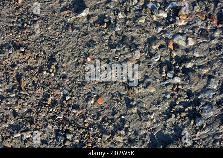Nature, minéraux, granit, pierres grises et miettes, petites briques rouges dispersées sur toute la surface sablonneuse de la terre. Banque D'Images