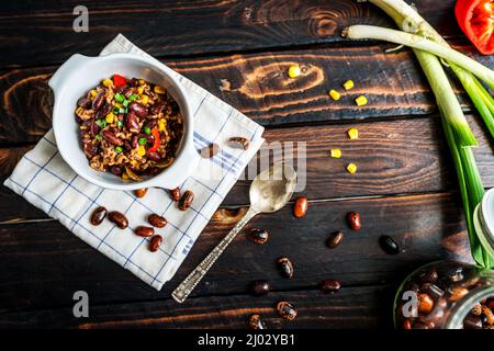 Chili mexicain ou Chili con carne. Haricots rouges cuits, viande hachée, piment, maïs et poivre dans une casserole sur une table en bois Banque D'Images