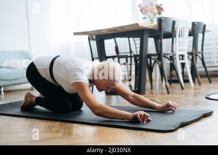 femme âgée faisant des exercices matinaux dans le salon. Banque D'Images