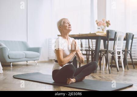 femme âgée méditant assise sur le sol dans son salon. Banque D'Images