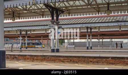 Gare de plates-formes avec un train en arrière-plan. Au-dessus de l'hôtel, vous trouverez des auvents historiques aux colonnes ornées. Deux personnes sont sur la plate-forme éloignée. Banque D'Images