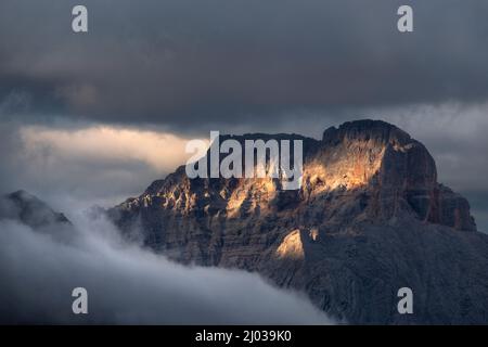 Coucher de soleil sur les montagnes de Croda Rossa d'Ampezzo entouré par le brouillard et l'obscurité avec seulement quelques spots de soleil, Dolomites, Vénétie, Italie, Europe Banque D'Images
