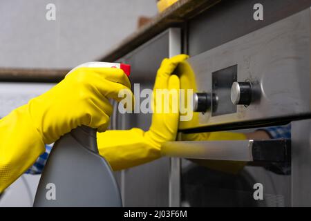 Les mains des femmes en gants de caoutchouc jaune frottent l'agent nettoyant sur la surface du four dans la cuisine. Concept de ménage et de ménage Banque D'Images