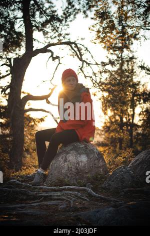 beau voyageur de brunette est assis au sommet d'une colline sur un rocher, se reposant après une forte montée. Coucher de soleil au sommet d'une montagne à Vuokatti, région de Kainuu Banque D'Images