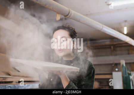 Charpentier soufflant de la sciure de bois dans l'atelier Banque D'Images