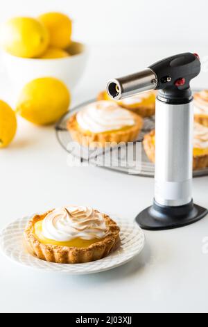 Tartelettes à la meringue au citron avec une lampe-torche pour faire dorer le dessus. Banque D'Images