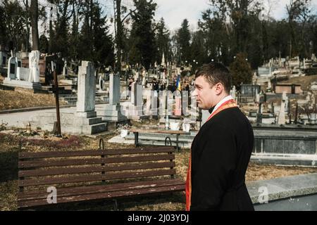 Lviv, Ukraine. 15th mars 2022. Un prêtre attend l'arrivée des cercueils des quatre soldats ukrainiens tués lors d'une frappe aérienne sur une base militaire à Yavariv, près de la frontière polonaise. Des boureurs se sont rassemblés au cimetière de Lychakivske à Lviv pour l'enterrement de quatre soldats ukrainiens; OLEH Yaschyshyn, Sergiy Melnyk, Rostyslav Romanchuk et Kyrylo Vyshyvany, qui ont été tués par une frappe aérienne russe au Centre international pour le maintien de la paix et la sécurité, une base militaire à Yavoriv près de la frontière polonaise plus tôt dans la semaine. (Photo par Matthew Hatcher/SOPA Images/Sipa USA) crédit: SIPA USA/Alay Live News Banque D'Images