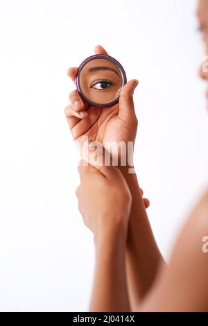 La beauté est dans l'œil du porte-bec. Photo studio d'une femme méconnaissable tenant un miroir de poche sur fond blanc. Banque D'Images