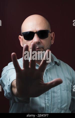 Portrait d'un homme barbu et chauve portant des lunettes sur un fond rouge foncé. Salvador, Bahia, Brésil. Banque D'Images