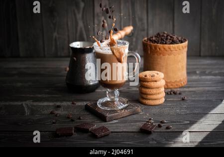 café avec crème aux éclaboussures et grains en vol avec biscuits sur fond sombre en bois Banque D'Images