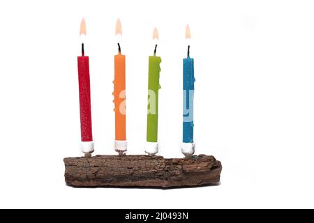 Gros plan d'un morceau de bois sur lequel quatre bougies d'anniversaire colorées différentes se tiennent sur fond blanc comme concept Banque D'Images