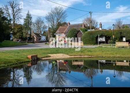 Cyclistes qui traversent le centre du village d'Oakley et l'étang à canards, Hampshire, Angleterre, Royaume-Uni Banque D'Images