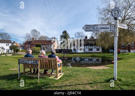 Oakley village centre, Hampshire, Angleterre, Royaume-Uni, avec des gens assis sur un banc près de l'étang de canard Banque D'Images