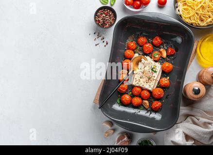 Pâtes au fromage feta cuites au four avec tomates cerises, ail et herbes sur fond gris. La recette de la fetopasta. Banque D'Images