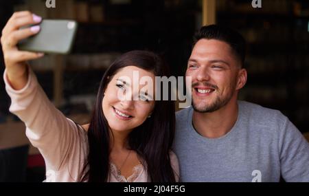 Le temps de selfie avec ma personne préférée. Photo courte d'un jeune couple qui prend un selfie tout en étant assis ensemble. Banque D'Images