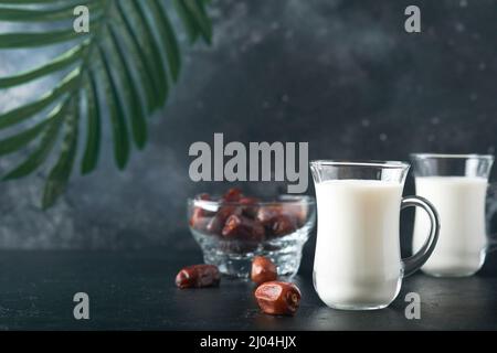 Plats et boissons du Kareem de Ramadan. Assiette de dattes, verre de lait et branche de palmier dattier sur fond noir. Un style de vie musulman juste. Plats végétariens. S Banque D'Images