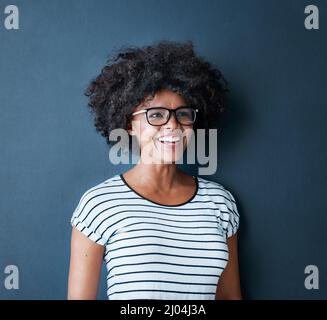 Voir le bon côté de la vie. Photo en studio d'une jeune femme attrayante et heureuse portant des lunettes sur fond bleu. Banque D'Images