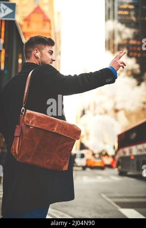 J'espère qu'un taxi me voit. Prise de vue d'un jeune homme joyeux écoutant de la musique tout en essayant de signaler un taxi pour se rendre au travail dans les rues animées de la ville. Banque D'Images