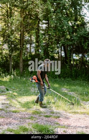 Homme noir utilisant un wacker de mauvaises herbes lors d'une journée d'été ensoleillée à Bridgeport, CT Banque D'Images