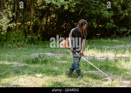 Homme noir avec des dreadlocks utilisant une mauvaise wacker sur sa ferme Banque D'Images