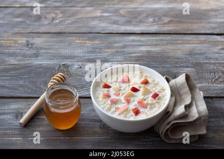 Bouillie de flocons d'avoine au lait avec pomme et miel dans un bol blanc sur une table en bois. Délicieux petit déjeuner maison sain Banque D'Images