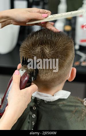 Coupe de cheveux pour enfants dans la barbershop, coupe de cheveux élégante et moderne pour les écoliers, travail pendant la pandémie, coupe de cheveux pour enfants avec des ciseaux. Banque D'Images