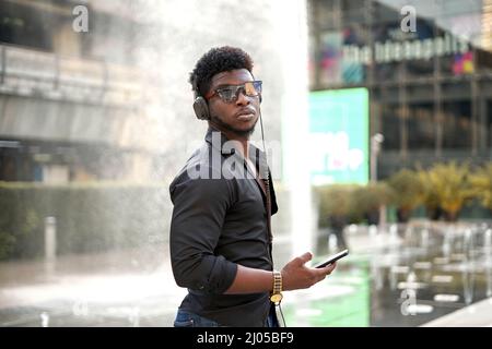 Homme africain sérieux tenant un mobile tout en écoutant de la musique à l'extérieur Banque D'Images