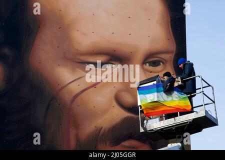 Fuorigrotta, Italie. 16th mars 2022. Travailleurs à l'intérieur d'un panier de grues mobiles avec le drapeau de la paix exposé, devant les Murales représentant le visage de l'écrivain et philosophe russe Fedor Dostoevskij, créé par l'artiste Jorit Agoch sur les murs de l'institut technique industriel de Righi à Fuorigrotta. Fuorigrotta, Italie, 16 mars 2022. (Photo par Vincenzo Izzo/Sipa USA) crédit: SIPA USA/Alay Live News Banque D'Images