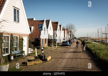 Cyclistes sur la route pavée passant par le village de Durgerdam, disposés le long de la digue juste au-dessus de l'eau, lors d'une journée ensoleillée de printemps, à Amsterdam, aux pays-Bas. Banque D'Images