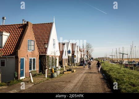 Les gens pédalent dans les rues pavées du village de Durgerdam, le long de la digue, juste au-dessus de l'eau, le jour ensoleillé du printemps, à Amsterdam, aux pays-Bas. Banque D'Images