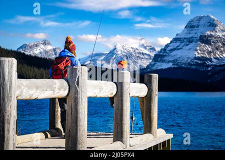 Deux enfants pêchent sur un quai avec des mains courantes en bois naturel surplombant un lac de montagne glacier près de Banff Canada dans la province de l'Alberta. Banque D'Images