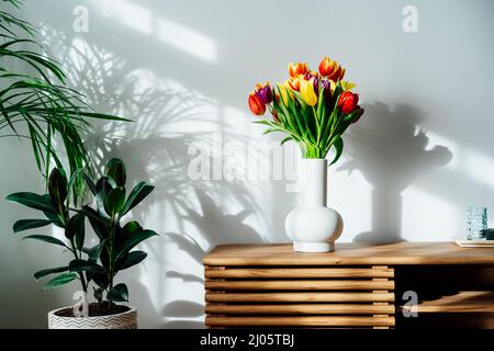 Intérieur scandinave avec bouquet de fleurs de tulipe coloré de printemps dans un vase en céramique debout sur une armoire en bois. Design minimaliste avec pl. Vert Banque D'Images