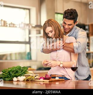La nourriture est amour pour votre estomac. Photo d'un jeune homme qui embrasse sa femme pendant qu'elle prépare le dîner. Banque D'Images