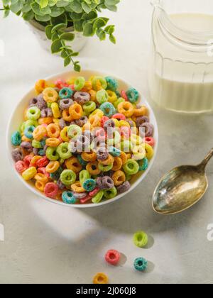 Anneaux de céréales aux fruits, cuillère et lait dans un pot sur fond blanc. Vue grand angle. Gros plan. Le concept est le grain entier petit déjeuner rapide. Aliments sucrés, Banque D'Images