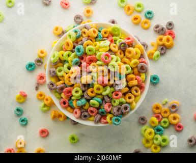 Vue de dessus. Beaucoup d'anneaux de céréales de fruits dans un bol et éparpillés sur la table sur un fond blanc. Petit déjeuner complet rapide. La nourriture préférée de Banque D'Images