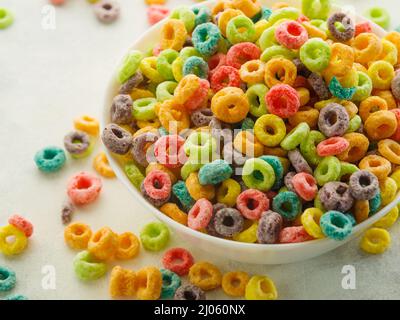 Prise de vue macro. Beaucoup de grains de fruits multi-couleurs anneaux dans un bol et près d'elle sur un fond blanc. Céréales petits déjeuners rapides, nourriture pour bébés, nourriture biologique, lui Banque D'Images