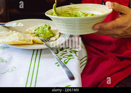 gros plan Homme caucasien argentin assis avec un bol en porcelaine avec guacamole à la main remplissant un arepa Banque D'Images