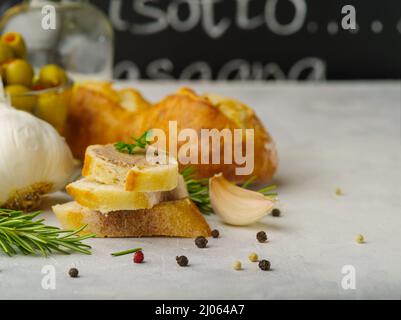 Appétissant foie gras de foie d'oie sur des tranches de baguette fraîche. Garni de branches de persil sur le dessus. Ail, légumes verts. Poivre noir sur fond blanc Banque D'Images