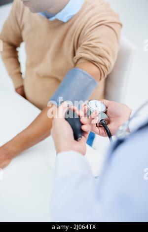 Contrôle de sa tension artérielle. Prise de vue en grand angle d'un médecin qui prend la tension artérielle d'un patient. Banque D'Images