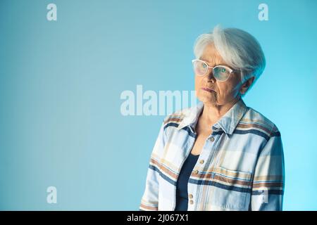 Photo en studio moyenne d'une femme caucasienne âgée à cheveux gris portant une chemise en flanelle et regardant malheureusement loin. Photo de haute qualité Banque D'Images