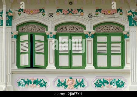 Beige Straits Chinese Peranakan shophouse avec volets en bois vert olive, motifs floraux rococo et miroir Bagua feng shui au-dessus du cadre Banque D'Images