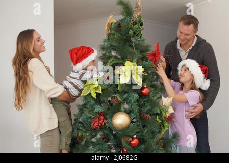 Préparez-vous pour les vacances. Photo d'un jeune garçon décorant un arbre de noël avec sa famille. Banque D'Images