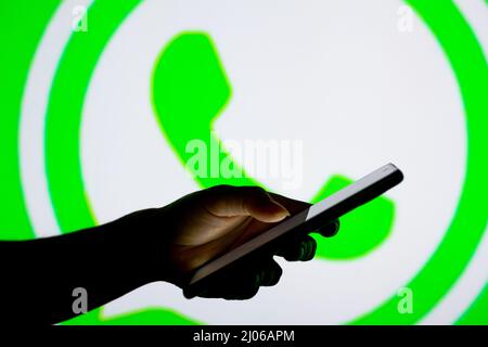 Dans cette illustration, le logo WhatsApp vu en arrière-plan d'une silhouette de femme tenant un téléphone mobile. Banque D'Images